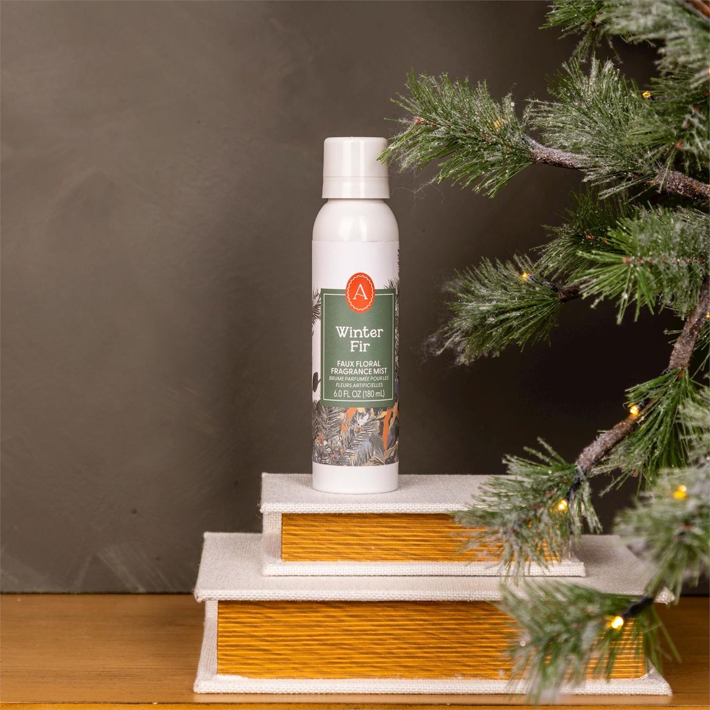 A can of 'Winter Fir' spray on a small wooden platform with a Christmas tree in the background.