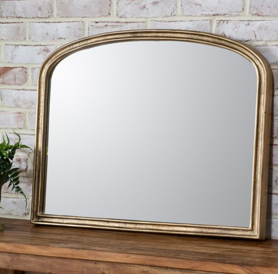 Gold-framed arched mirror on a wooden surface with a brick wall background