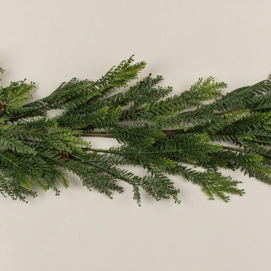 A green artificial pine garland with dense, needle-like foliage, laid horizontally across a plain off-white background.