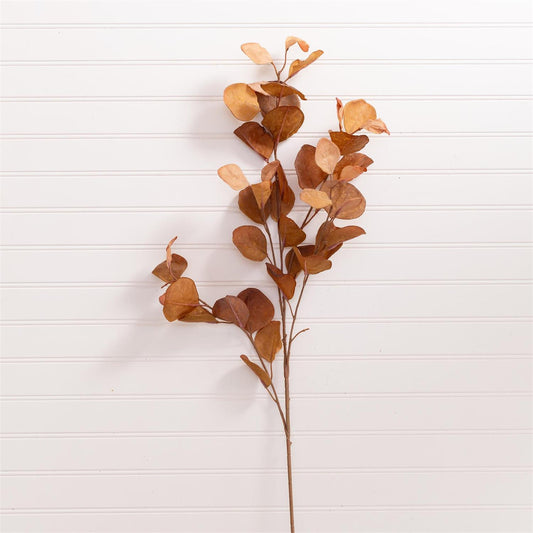 Artificial brown leaf branch on a white wooden surface
