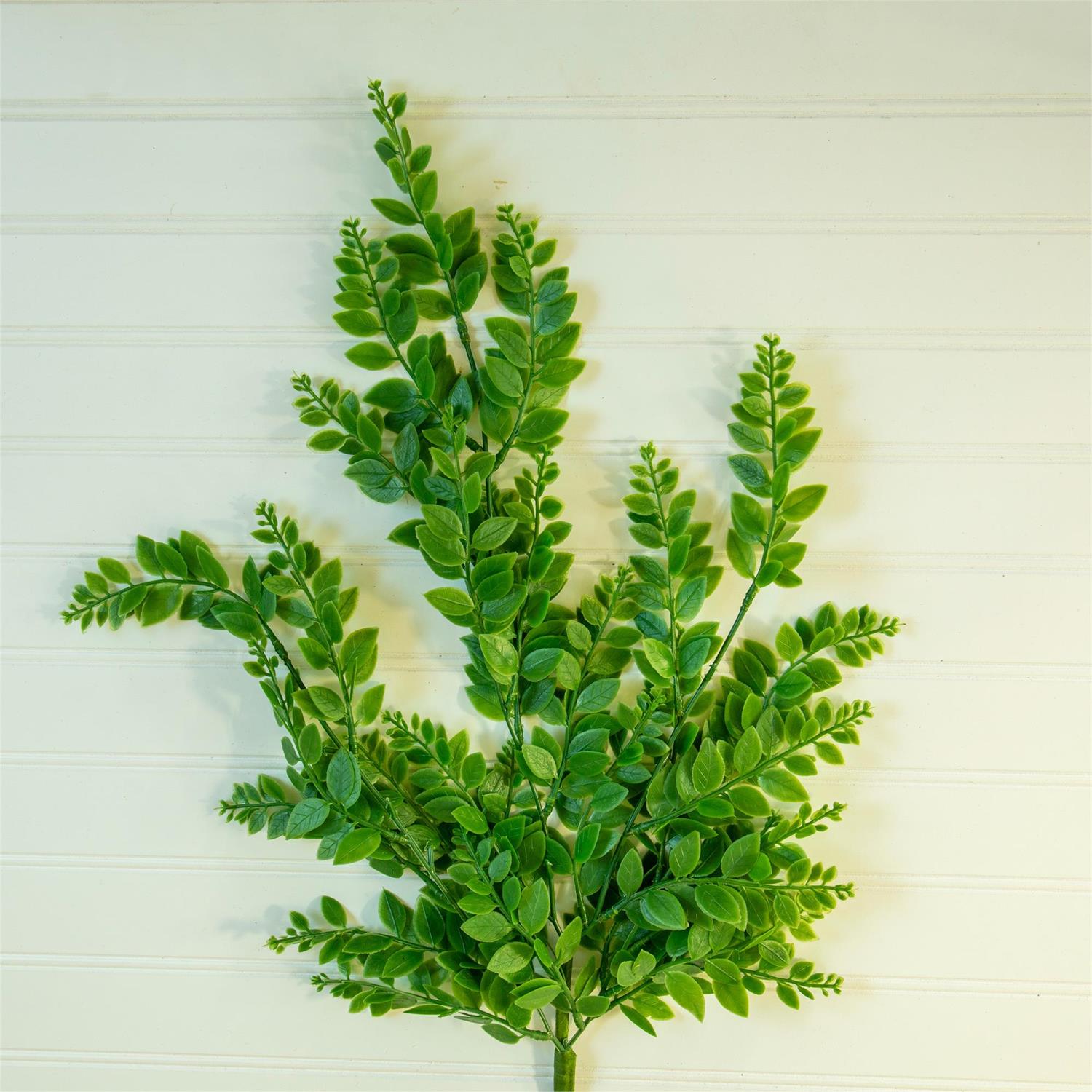 Artificial green leaf branch on a light wooden background