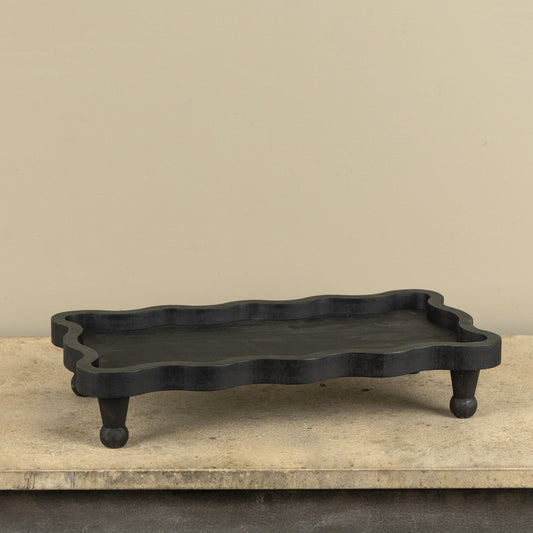 Black wavy-edged tray on a wooden surface with a beige background