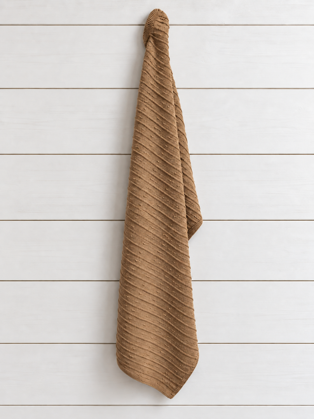 A ribbed camel cotton towel hanging vertically against a white wood plank wall.