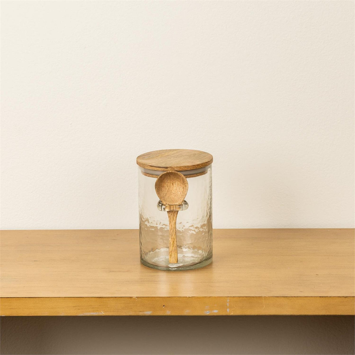 Clear glass jar with wooden lid and spoon on a wooden surface
