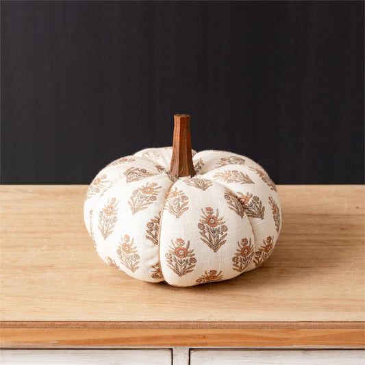 Decorative pumpkin with orange and brown floral pattern and cream color cloth on a wooden surface