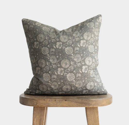 Floral patterned pillow on a wooden stool against a white background