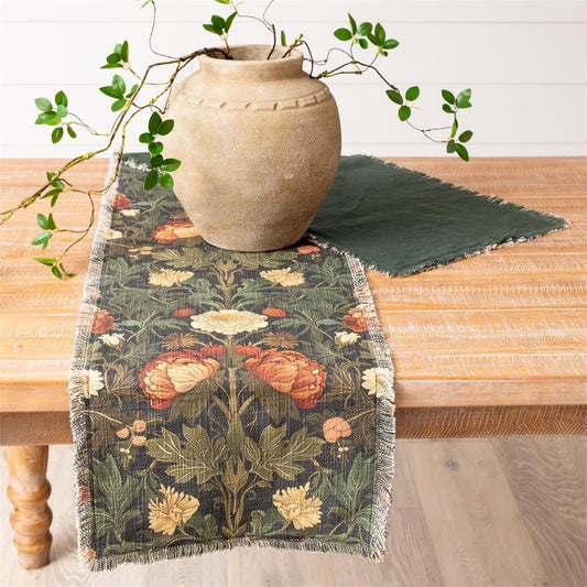 Floral table runner on a wooden table with a vase and leaves.