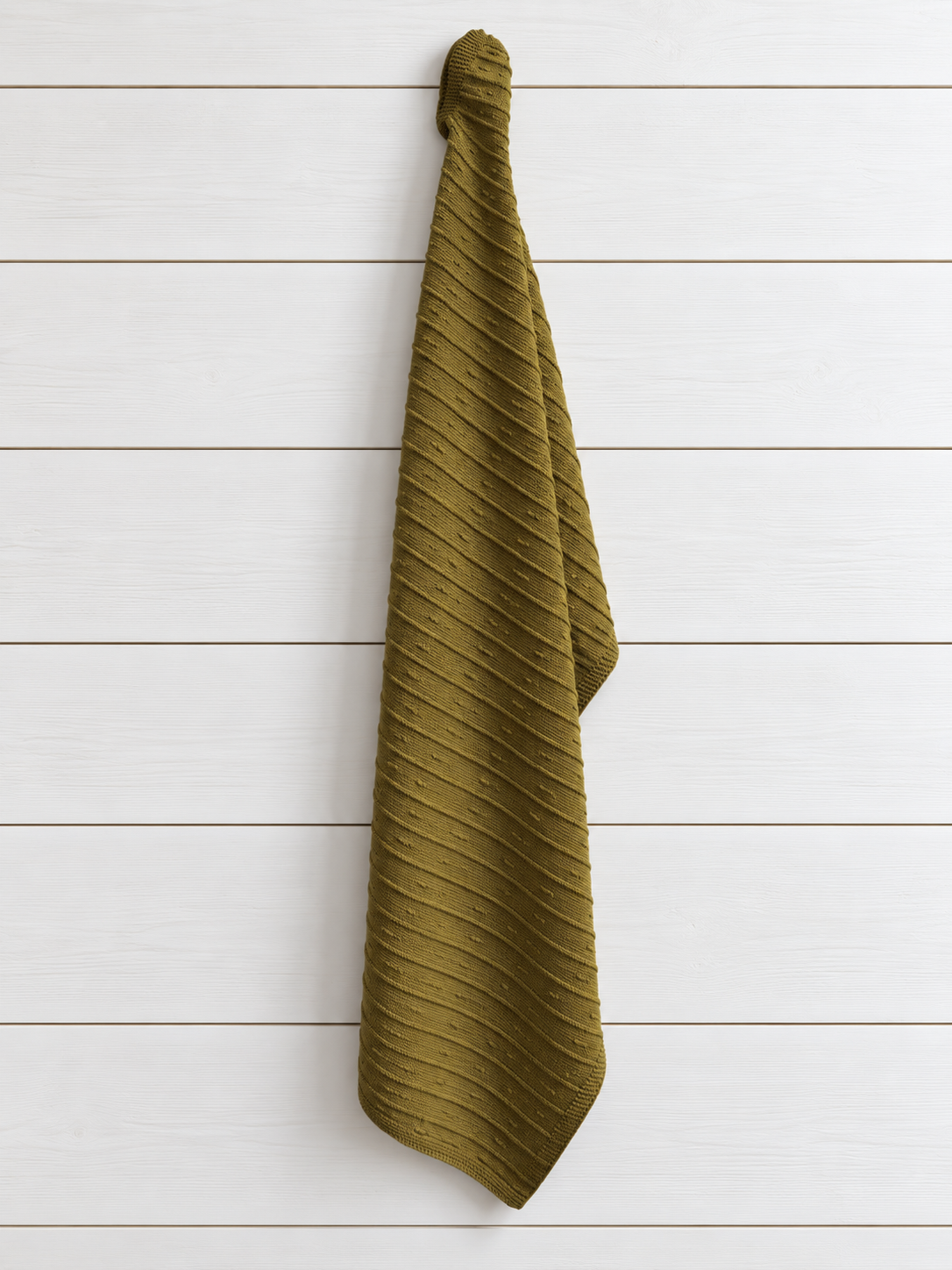 An olive green ribbed knit baby towel hanging from a hook against a white wood plank wall.