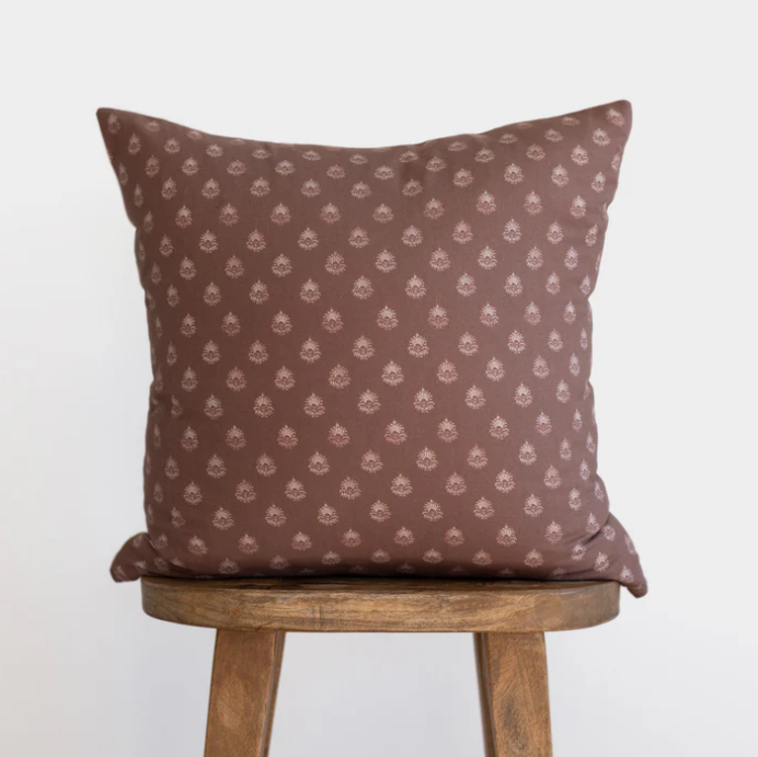 Brown pillow with a subtle pattern on a wooden stool against a white background