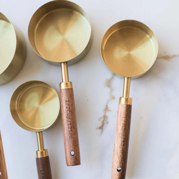 Set of brass measuring cups with wooden handles on a marble surface