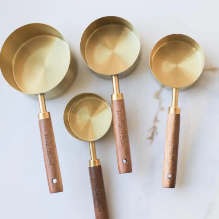 Set of brass measuring cups with wooden handles on a white surface