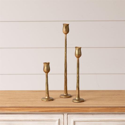 Three gold candle holders on a wooden surface with a white paneled background