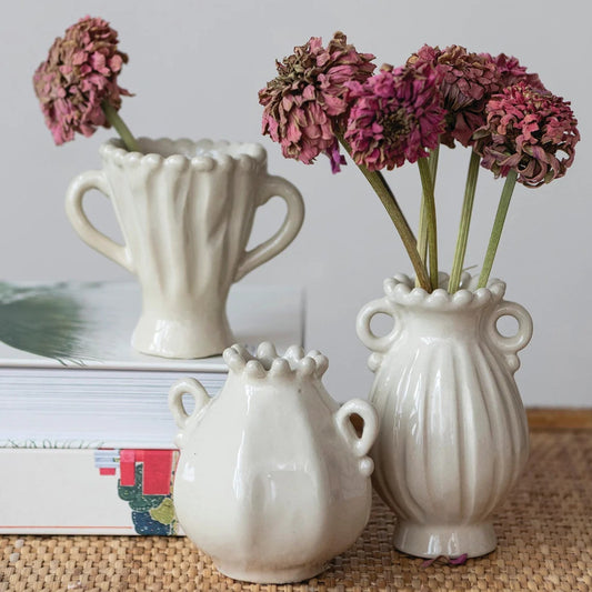 Three white ceramic vases with floral arrangements on a textured surface.