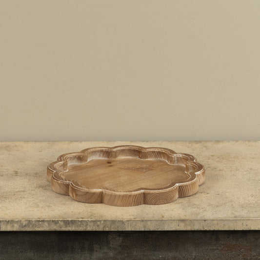 Wooden tray with scalloped edges on a  beige countertop and background.