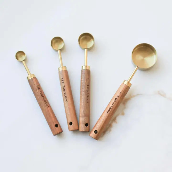 Set of four brass measuring cups with wooden handles on a marble surface