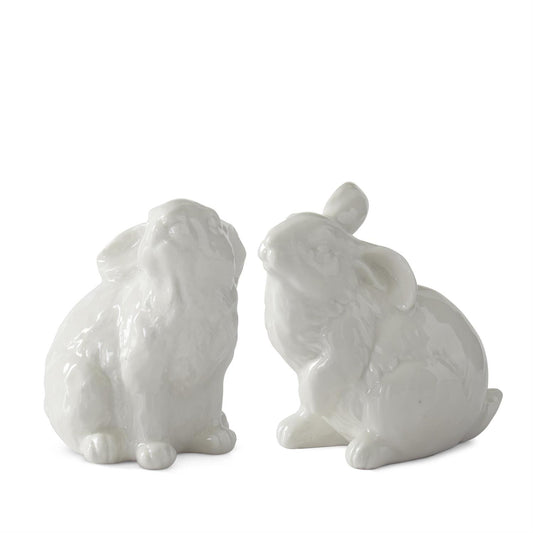 Two white ceramic rabbit figurines sitting position looking up on a white background