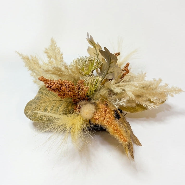 A dried floral arrangement featuring beige pampas grass, brown and tan leaves, small orange-brown seed clusters, and a soft cream puff, photographed on a plain white background.
