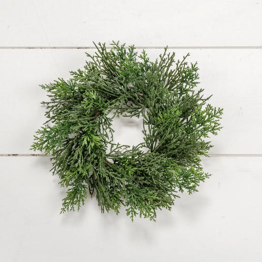 An artificial green evergreen wreath with dense, textured foliage, displayed against a white wood plank background.
