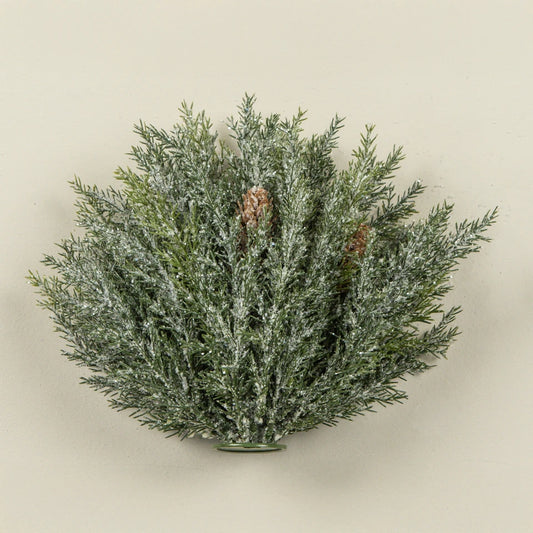 An artificial flocked pine wreath with green needles dusted in white snow-like powder and small brown pinecones, shown against a plain beige background.