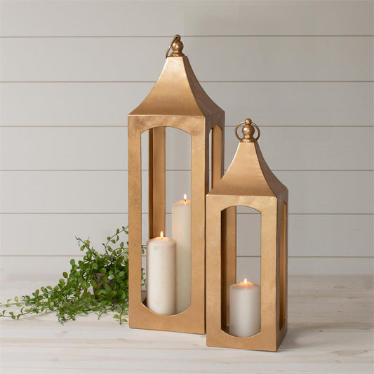 Two gold lanterns with candles inside on a wooden surface with a light background