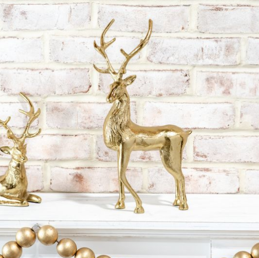 A gold metallic deer figurine stands on a white mantel in front of a white brick wall.