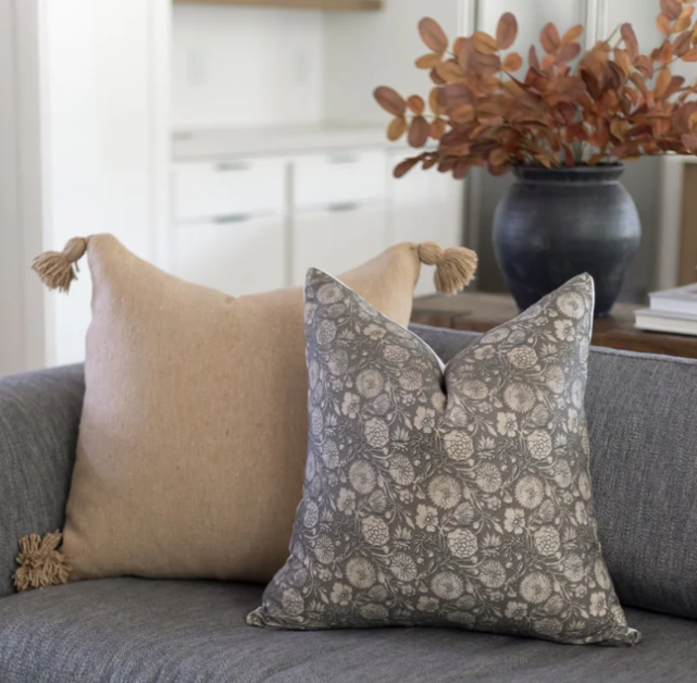 Two decorative pillows on a sofa with a vase of flowers in the background.