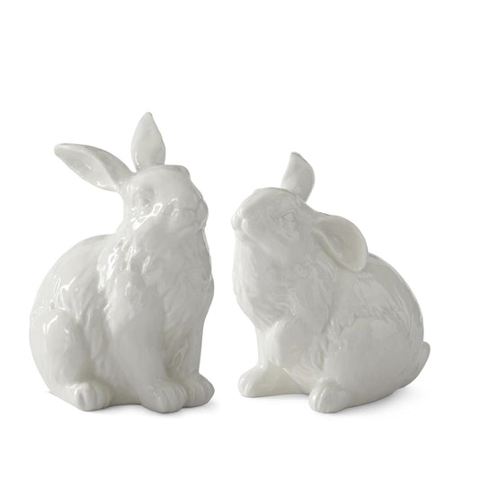 Two white small ceramic rabbit figurines both in sitting positions on a white background