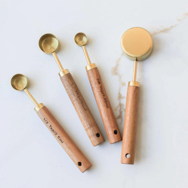 Set of five wooden measuring cups with brass handles on a light background